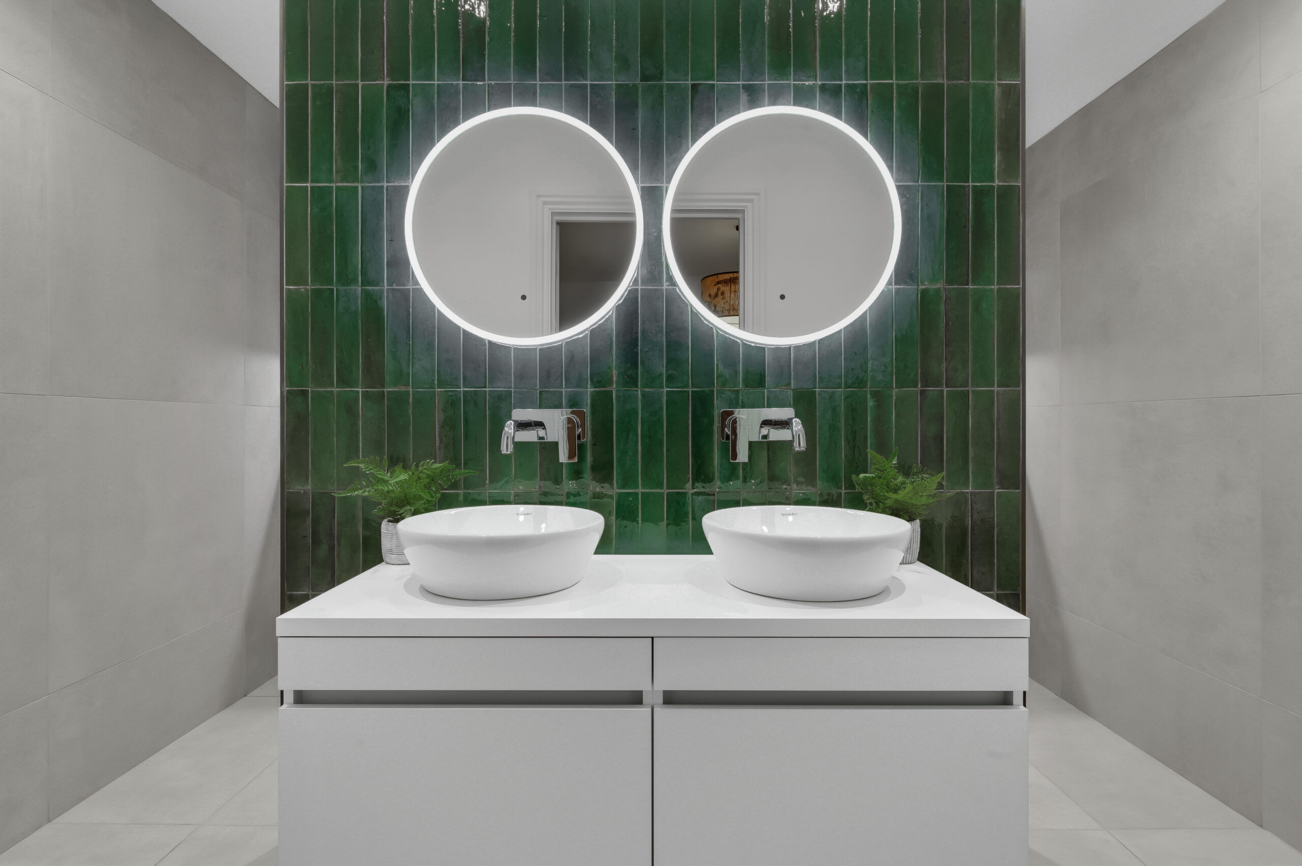 Double vanity with two vessel basins, round illuminated mirrors and glossy green feature tiles